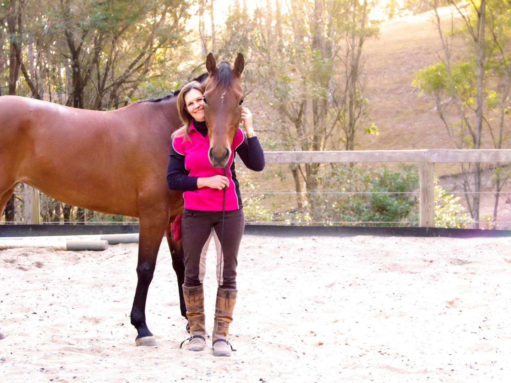 a woman holding a brown horse standing next to a fence
