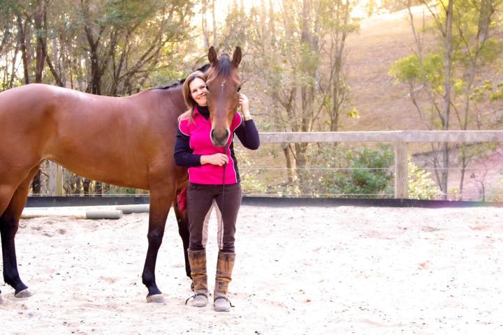 a woman holding a brown horse standing next to a fence