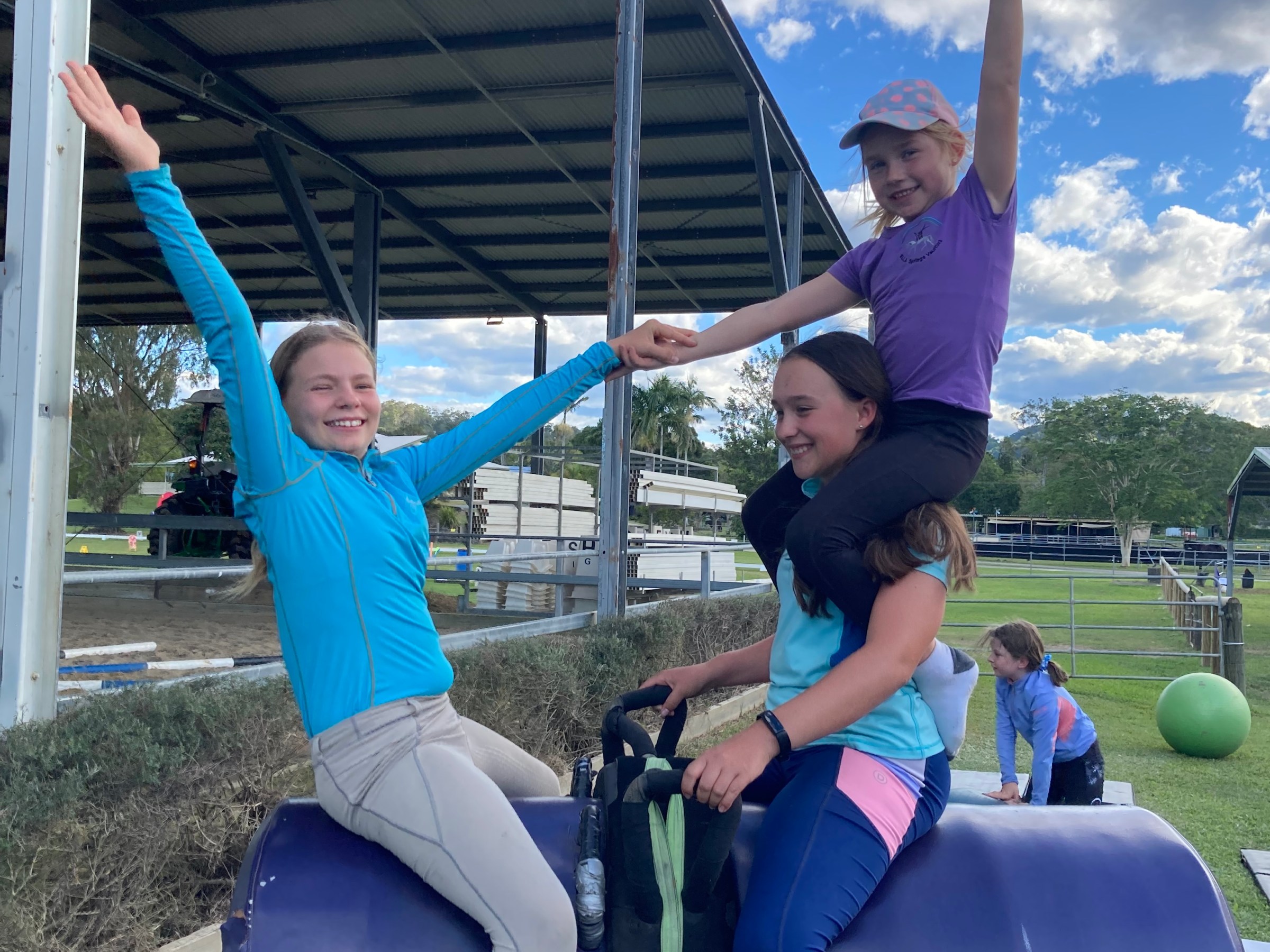 Three people joyfully balancing on a padded structure outdoors.